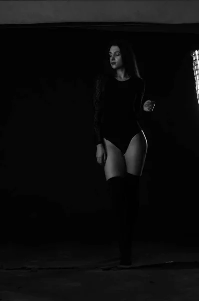 美しいですブルネット若いです女性で黒ボディスーツPosingオンダークスタジオの背景 — ストック写真