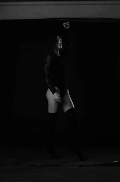 穿着黑色紧身衣的漂亮的黑发女青年在黑暗的工作室背景下摆姿势 — 图库照片