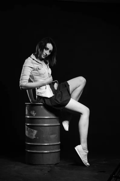 beautiful woman with short hear in stylish clothes posing with barrel on dark studio background