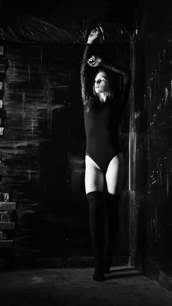 Молода жінка в чорному комбінезоні позує на темному тлі, чорне волосся і м'язистої спортивної фігури . — стокове фото