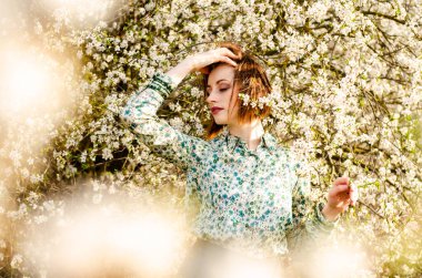 Açık havada şeftali çiçekleriyle poz veren güzel, gülümseyen genç kadın.