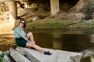 Güneşli bir günde nehir kıyısında şık kıyafetler içinde poz veren güzel esmer kadın.