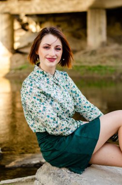 Güneşli bir günde nehir kıyısında şık kıyafetler içinde poz veren güzel esmer kadın.