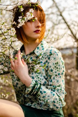 Açık havada şeftali çiçekleriyle poz veren güzel, gülümseyen genç kadın.