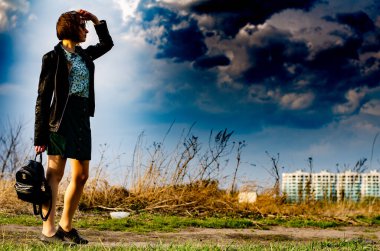 Güzel esmer kadın, arka planda şehir manzarası olan çayırda şık giysiler içinde poz veriyor.