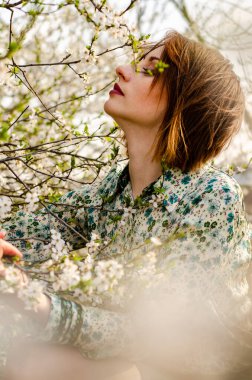Açık havada şeftali çiçekleriyle poz veren güzel, gülümseyen genç kadın.