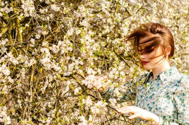 Açık havada şeftali çiçekleriyle poz veren güzel, gülümseyen genç kadın.