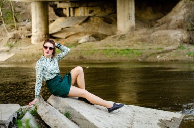 Güneşli bir günde nehir kıyısında şık kıyafetler içinde poz veren güzel esmer kadın.