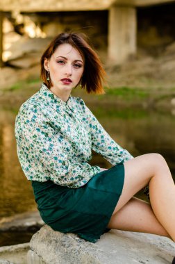 Güneşli bir günde nehir kıyısında şık kıyafetler içinde poz veren güzel esmer kadın.