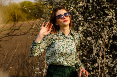 Açık havada şeftali çiçekleriyle poz veren güzel, gülümseyen genç kadın.