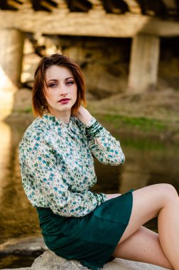 Güneşli bir günde nehir kıyısında şık kıyafetler içinde poz veren güzel esmer kadın.