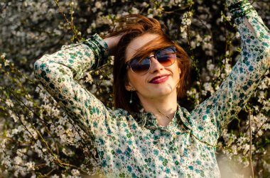 Açık havada şeftali çiçekleriyle poz veren güzel, gülümseyen genç kadın.