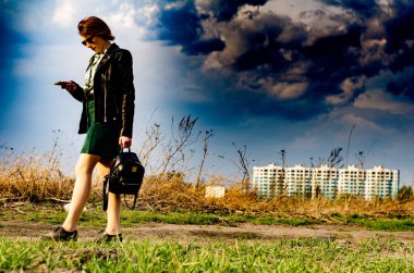 Güzel esmer kadın, arka planda şehir manzarası olan çayırda şık giysiler içinde poz veriyor.