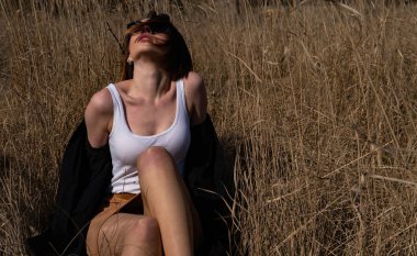 Güzel kızıl saçlı bir kızın çimlerin üzerinde yatması, poz vermesi, kucaklaması. Sarı otlu sonbahar ormanı. Uzun saçlı kadın..