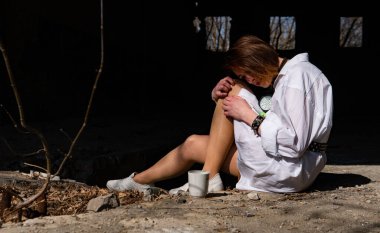 Terk edilmiş bir yerde oturan beyaz gömlekli güzel bir kadın.