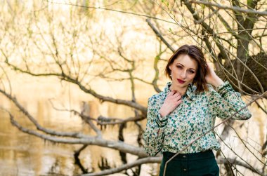 Güneşli bir günde nehir kıyısında şık kıyafetler içinde poz veren güzel esmer kadın.