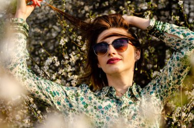 Açık havada şeftali çiçekleriyle poz veren güzel, gülümseyen genç kadın.