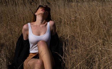 Güzel kızıl saçlı bir kızın çimlerin üzerinde yatması, poz vermesi, kucaklaması. Sarı otlu sonbahar ormanı. Uzun saçlı kadın..