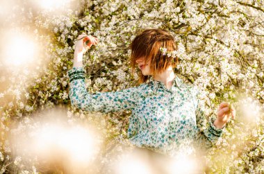 Açık havada şeftali çiçekleriyle poz veren güzel, gülümseyen genç kadın.