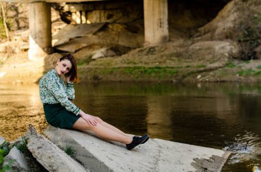 Güneşli bir günde nehir kıyısında şık kıyafetler içinde poz veren güzel esmer kadın.