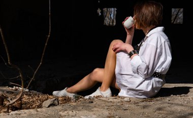 Terk edilmiş bir yerde oturan beyaz gömlekli güzel bir kadın.