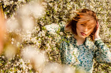 Açık havada şeftali çiçekleriyle poz veren güzel, gülümseyen genç kadın.