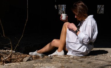 Terk edilmiş bir yerde oturan beyaz gömlekli güzel bir kadın.