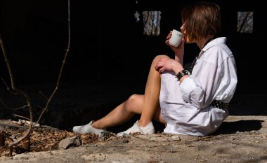 Terk edilmiş bir yerde oturan beyaz gömlekli güzel bir kadın.