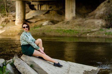 Güneşli bir günde nehir kıyısında şık kıyafetler içinde poz veren güzel esmer kadın.
