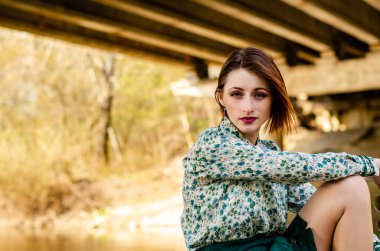 Güneşli bir günde nehir kıyısında şık kıyafetler içinde poz veren güzel esmer kadın.