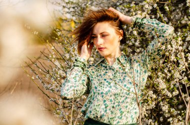 Açık havada şeftali çiçekleriyle poz veren güzel, gülümseyen genç kadın.