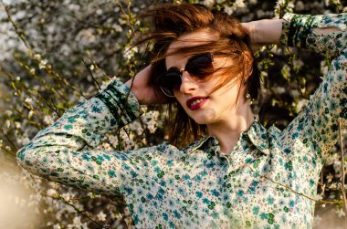 Açık havada şeftali çiçekleriyle poz veren güzel, gülümseyen genç kadın.