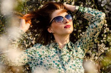 Açık havada şeftali çiçekleriyle poz veren güzel, gülümseyen genç kadın.