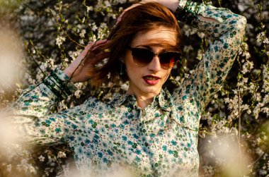 Açık havada şeftali çiçekleriyle poz veren güzel, gülümseyen genç kadın.