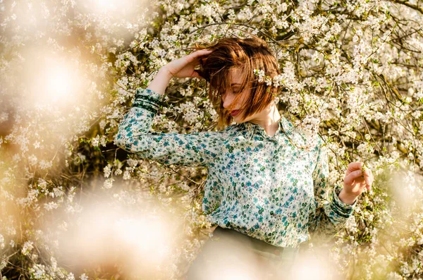 Açık havada şeftali çiçekleriyle poz veren güzel, gülümseyen genç kadın.
