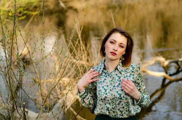 Güneşli bir günde nehir kıyısında şık kıyafetler içinde poz veren güzel esmer kadın.