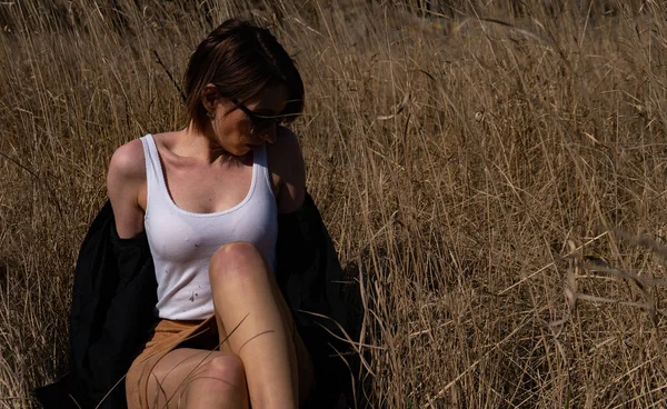 Güzel kızıl saçlı bir kızın çimlerin üzerinde yatması, poz vermesi, kucaklaması. Sarı otlu sonbahar ormanı. Uzun saçlı kadın..