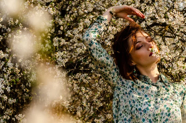 Açık havada şeftali çiçekleriyle poz veren güzel, gülümseyen genç kadın.