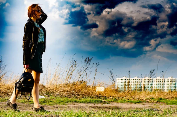 Güzel esmer kadın, arka planda şehir manzarası olan çayırda şık giysiler içinde poz veriyor.