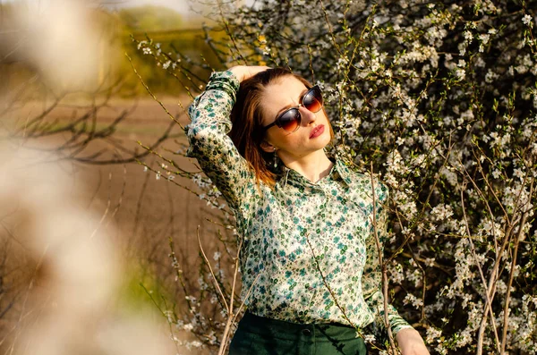 Açık havada şeftali çiçekleriyle poz veren güzel, gülümseyen genç kadın.