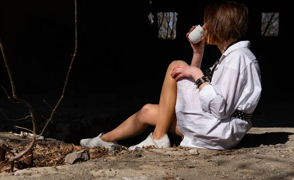 Terk edilmiş bir yerde oturan beyaz gömlekli güzel bir kadın.