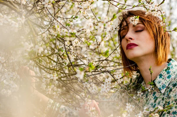 Açık havada şeftali çiçekleriyle poz veren güzel, gülümseyen genç kadın.