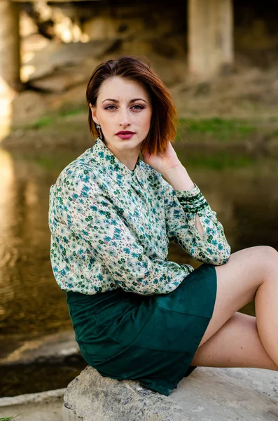 Güneşli bir günde nehir kıyısında şık kıyafetler içinde poz veren güzel esmer kadın.