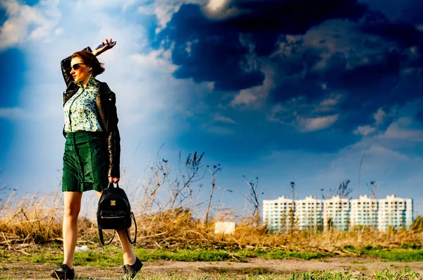 Güzel esmer kadın, arka planda şehir manzarası olan çayırda şık giysiler içinde poz veriyor.