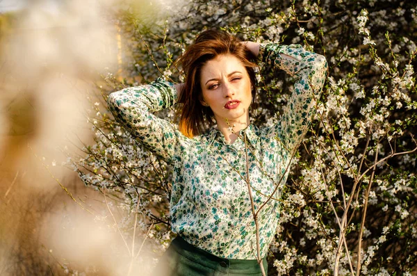 Açık havada şeftali çiçekleriyle poz veren güzel, gülümseyen genç kadın.