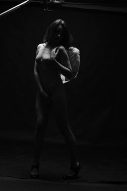 Dekoratif melek kanatları takan çıplak bir kadın. Karanlık arka planda poz veriyor.    