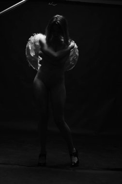 Dekoratif melek kanatları takan çıplak bir kadın. Karanlık arka planda poz veriyor.    