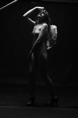 Dekoratif melek kanatları takan çıplak bir kadın. Karanlık arka planda poz veriyor.    