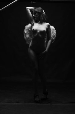 Dekoratif melek kanatları takan çıplak bir kadın. Karanlık arka planda poz veriyor.    