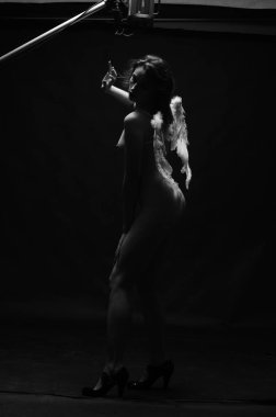 Dekoratif melek kanatları takan çıplak bir kadın. Karanlık arka planda poz veriyor.    